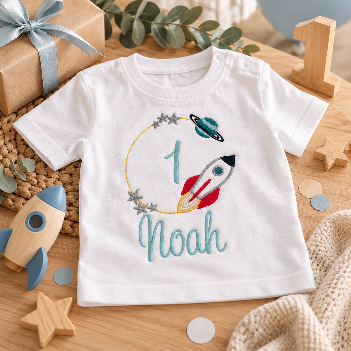 Weißes Geburtstagsshirt zum 1. Geburtstag mit Rakete, Zahl 1 und Name Noah, dekoriert mit Holzsternen und Geschenk.