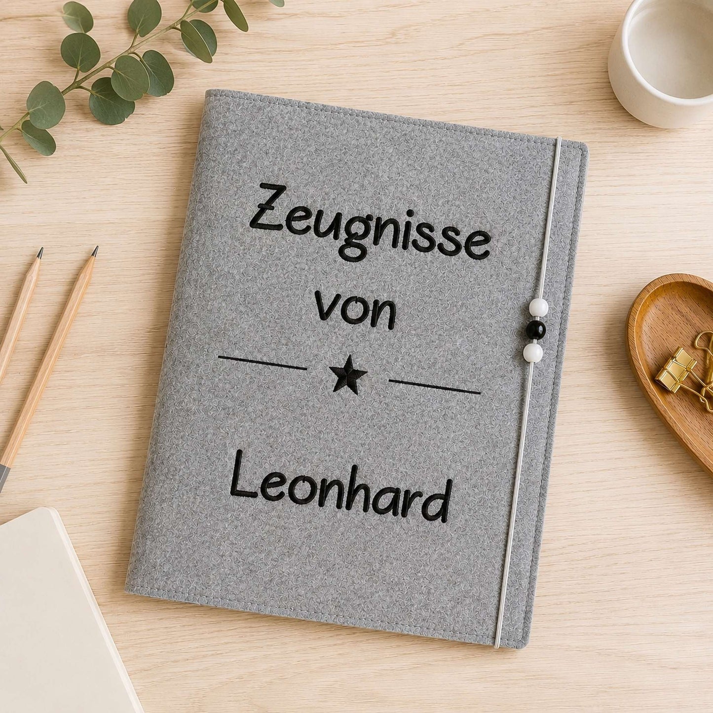 Personalisierte Zeugnismappe aus grauem Filz mit hochwertiger Namensstickerei und Gummibandverschluss zur Aufbewahrung von Schulzeugnissen.