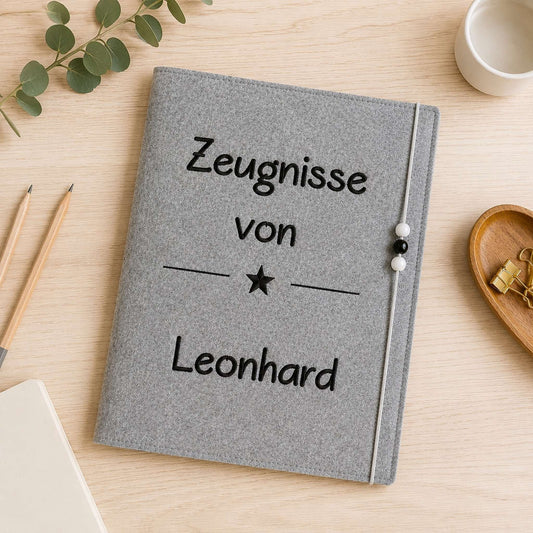 Personalisierte Zeugnismappe aus grauem Filz mit hochwertiger Namensstickerei und Gummibandverschluss zur Aufbewahrung von Schulzeugnissen.