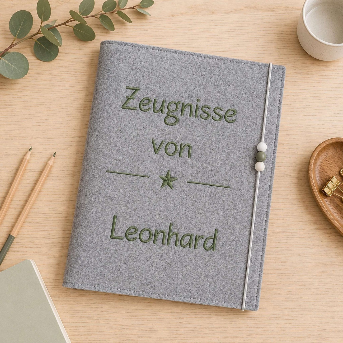 Personalisierte Zeugnismappe aus grauem Filz mit moosgrüner Namensstickerei und Sternmotiv als Geschenk zur Einschulung.